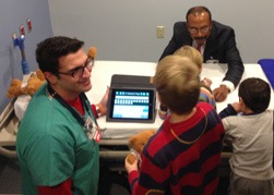 At the gathering to launch the new pediatric room at the Columbia Memorial Hospital Emergency Department in Hudson, Frank Saladino, RN, introduces some youngsters to iPad apps intended to help kids with autism spectrum disorders communicate with caregivers in case of a medical emergency. Across the bed is Dr. Arun Nandi, director of the department. The new room opened this week. Photo by Parry Teasdale.